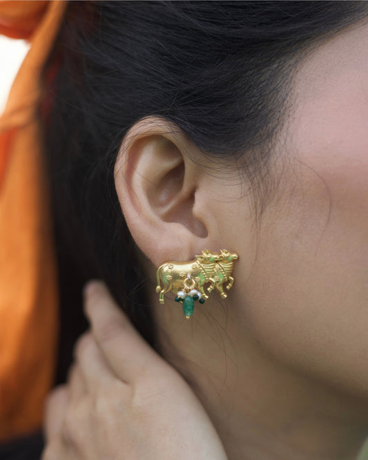 Close-up of gold-polished 925 silver cow motif stud earrings with pearl clusters and green stone drops on a white background.