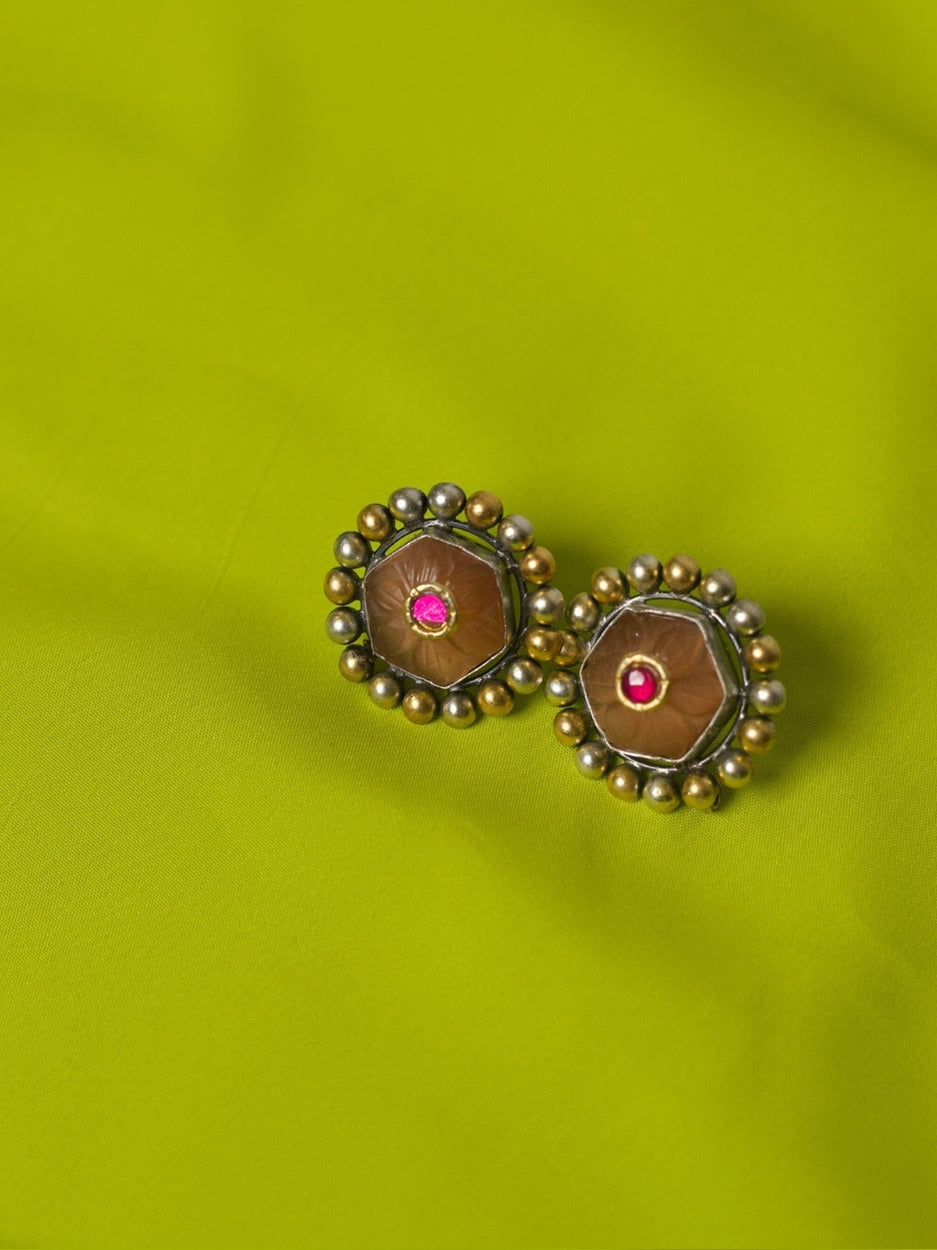 Close-up of handmade 925 silver Mango Pudding Studs with golden and silver beaded frame and pink crystal centre on green fabric.