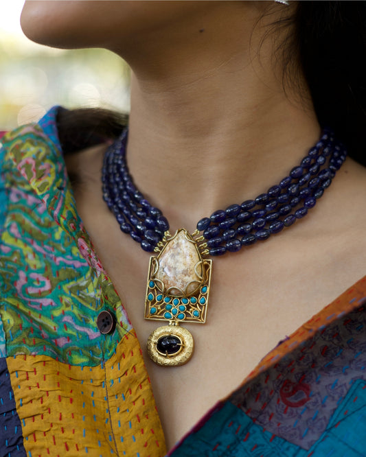 Four-strand indigo bead necklace in 925 silver with large marbled stone pendant, turquoise accents, and hammered gold drop detail.
