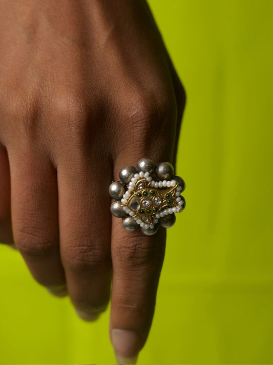Close-up of 92.5 silver fish motif ring with pearl and silver ball border, worn on hand against lime green background.