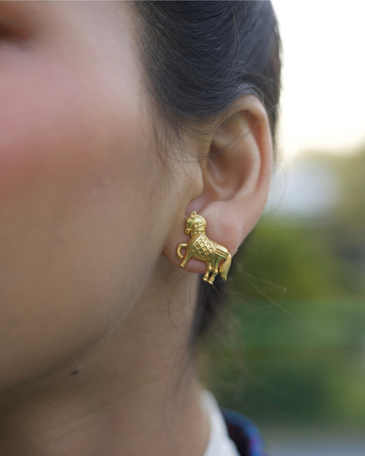 Small gold horse stud earrings with prancing leg and detailed saddle texture, polished finish, on ear.