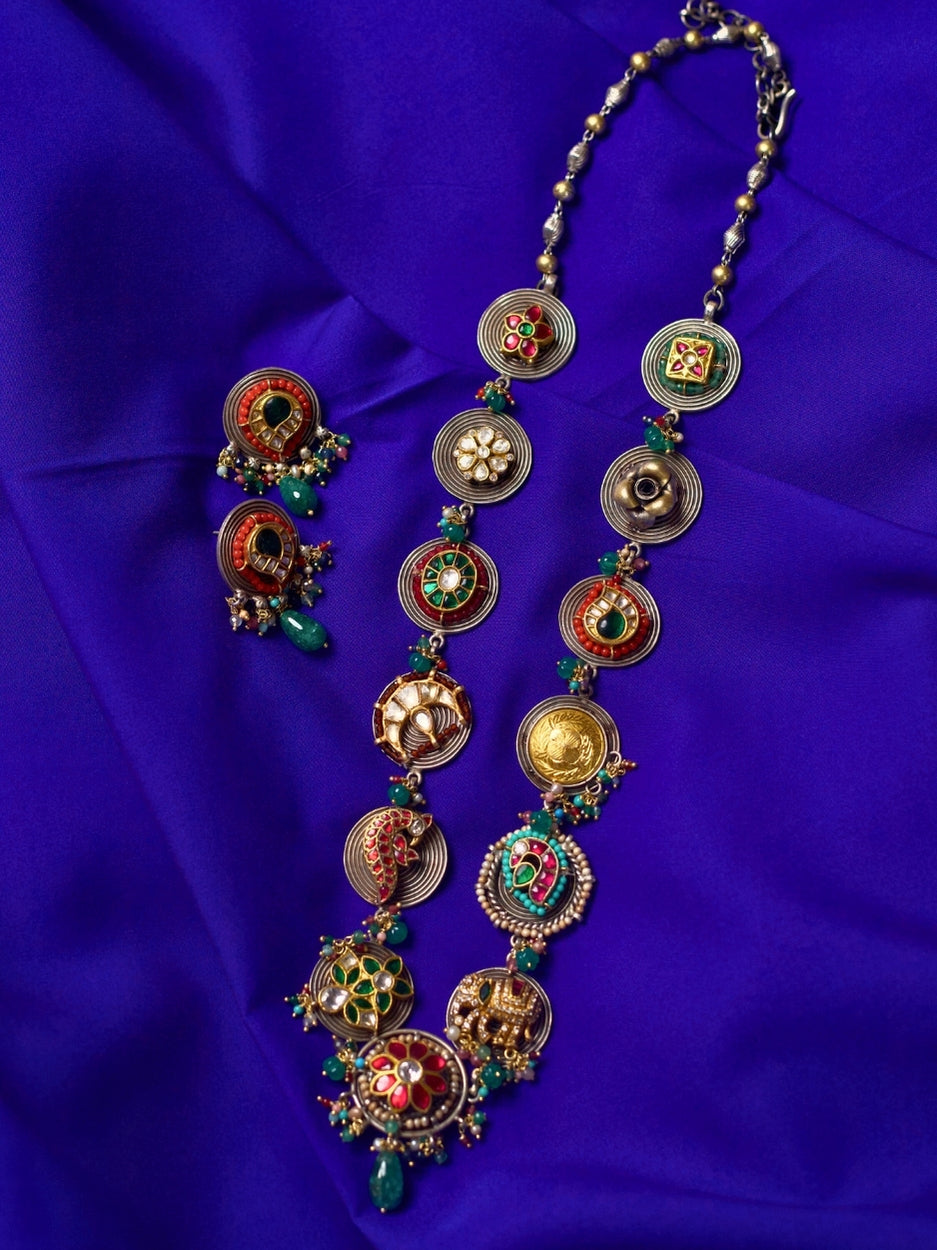 The Maharani Medley Necklace Set in 92.5 silver featuring circular medallion forms, kundan stones, enamel detailing, moissanite accents, and matching earrings – styled on model in deep blue outfit.