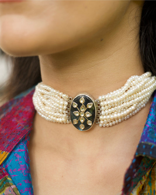 Model wearing layered pearl choker in 925 silver with oval oxidised centre and gold-polished kundan floral motif.