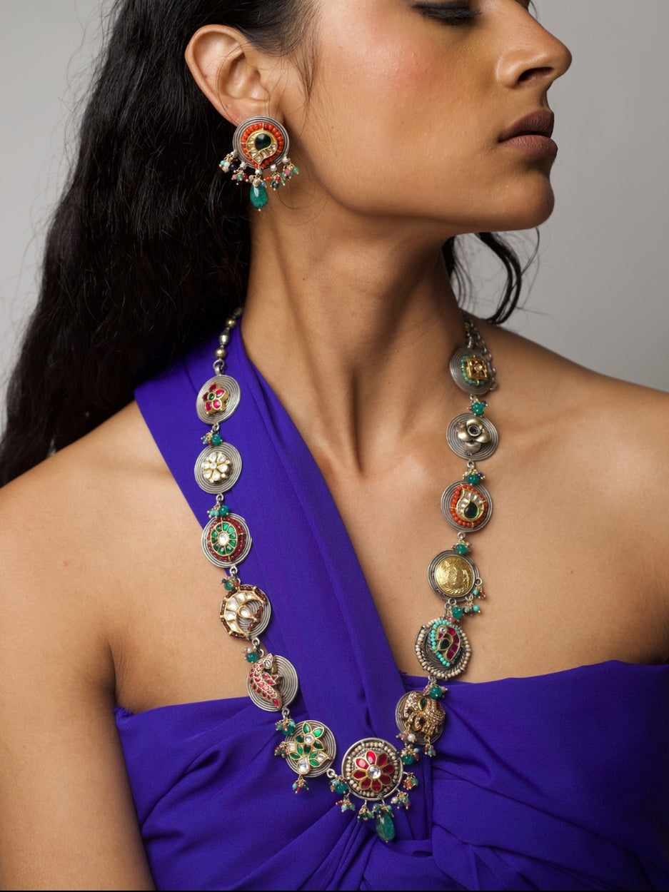 The Maharani Medley Necklace Set in 92.5 silver featuring circular medallion forms, kundan stones, enamel detailing, moissanite accents, and matching earrings – styled on model in deep blue outfit.