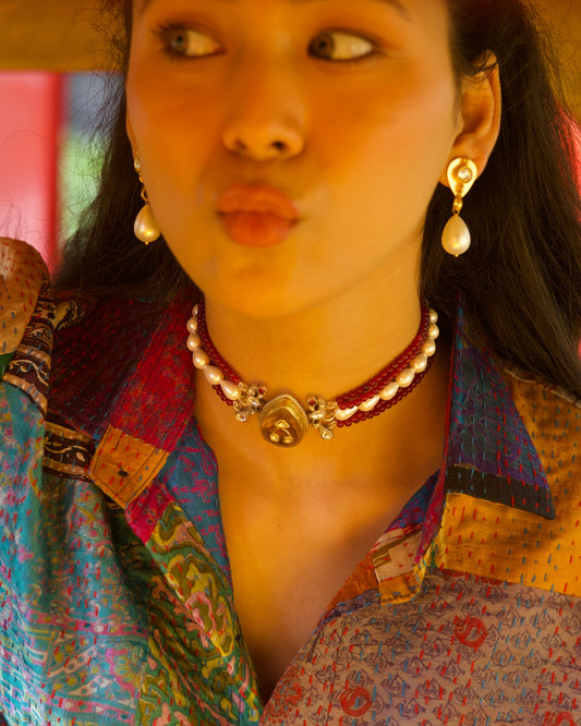 Multi-strand red bead choker in 925 silver with gold polish, pearl accents, and a large honey-toned teardrop stone centre pendant, on neck.