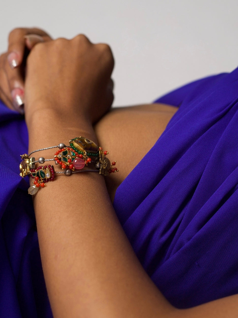 Handcrafted 92.5 silver bracelet with enamel folk charms, cow motif, and tribal bead detailing – styled on wrist against purple background.