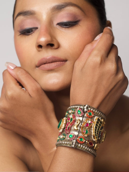 Close-up of Bazaar Relic Cuff in 92.5 silver featuring tribal base, gold motifs, emerald green stone, pearls, and red-green tikdas — worn on wrist