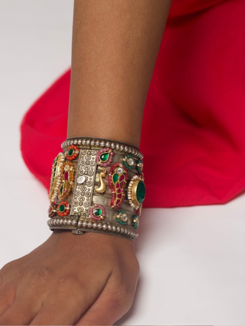 Close-up of Bazaar Relic Cuff in 92.5 silver featuring tribal base, gold motifs, emerald green stone, pearls, and red-green tikdas — worn on wrist