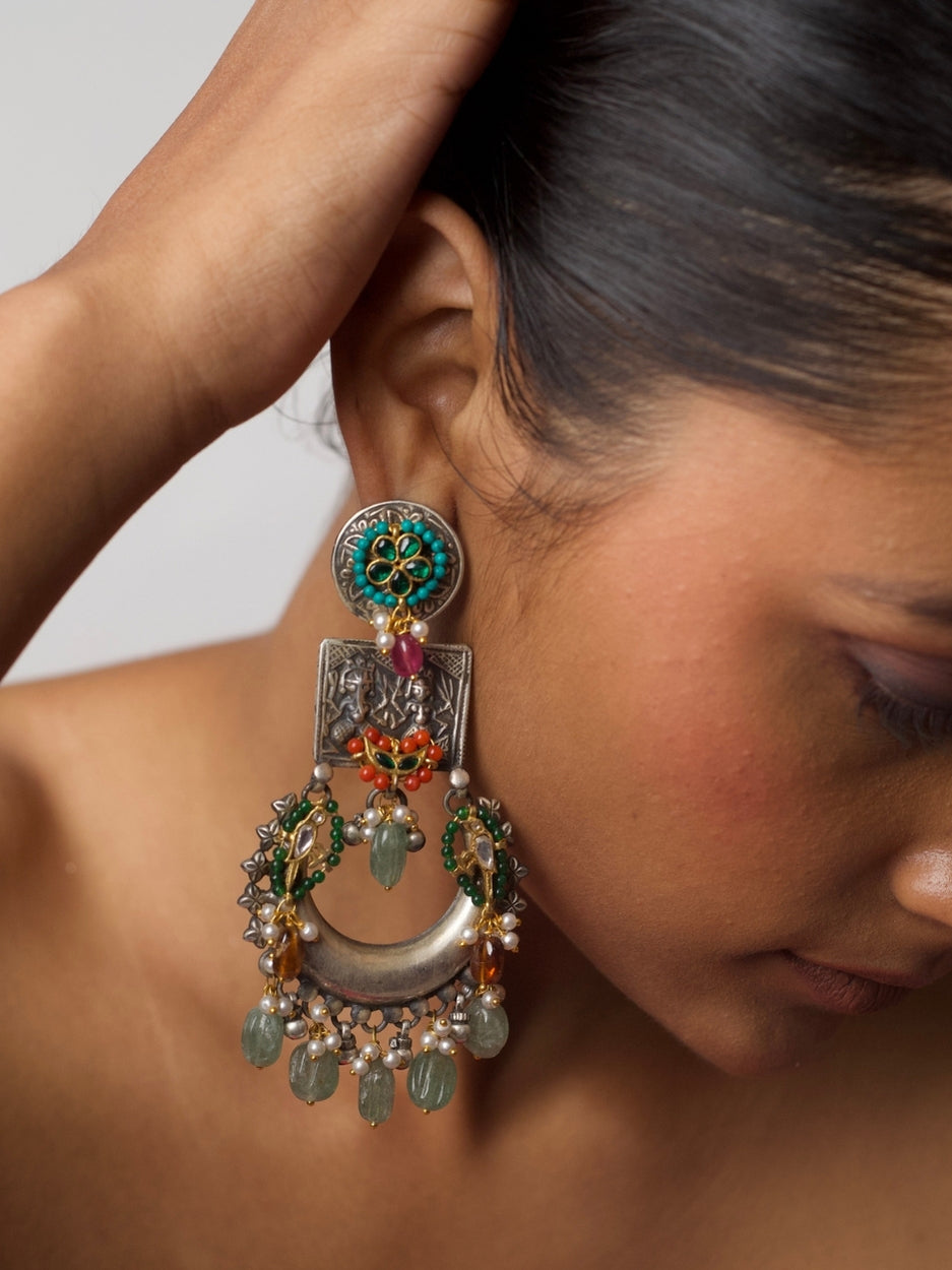 Close-up of Naksa’s Prachin Pakshi Chaandbaalis in pure silver, featuring tribal carvings, floral enamel, golden birds, gemstone drops, and crescent motifs.