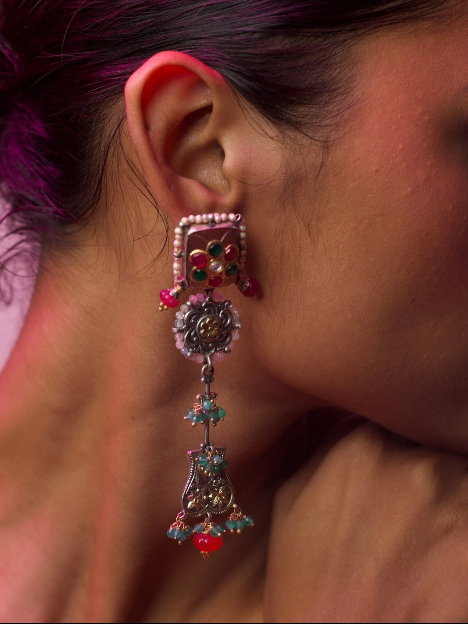 Close-up of a woman wearing Pretty Peculiar Earrings in pure 92.5 silver, featuring layered design with pearl-framed red and green enamel stud, oxidised silver floral centre, and dangling ornate drop with green and pink beads.
