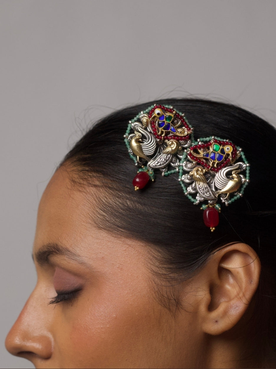 Close-up of statement 92.5 silver earrings featuring bird motifs in two-tone silver-gold and kundan-style colored enamel, bordered with mint green beads and a dangling red bead drop.