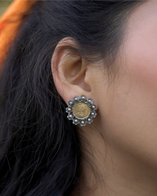 Close-up of dual-tone 925 silver stud earrings featuring an embossed vintage coin centre with oxidised floral petal border and bead detailing, worn on ear.