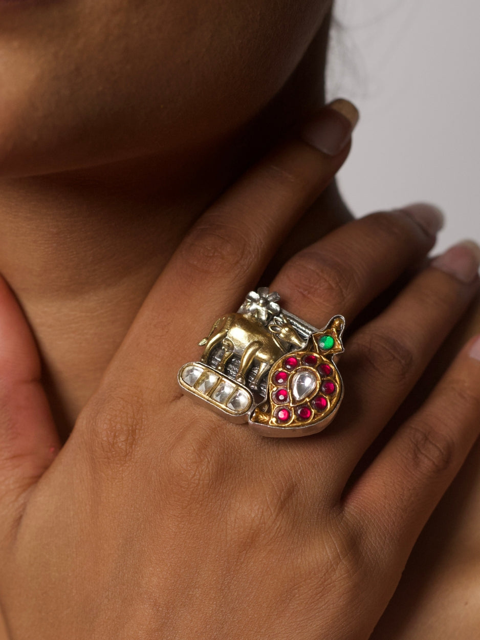 Close-up of a handcrafted 92.5 silver fusion ring with a golden cow, crescent paisley motif, and red-green gemstone detailing, inspired by Pichwai art.
