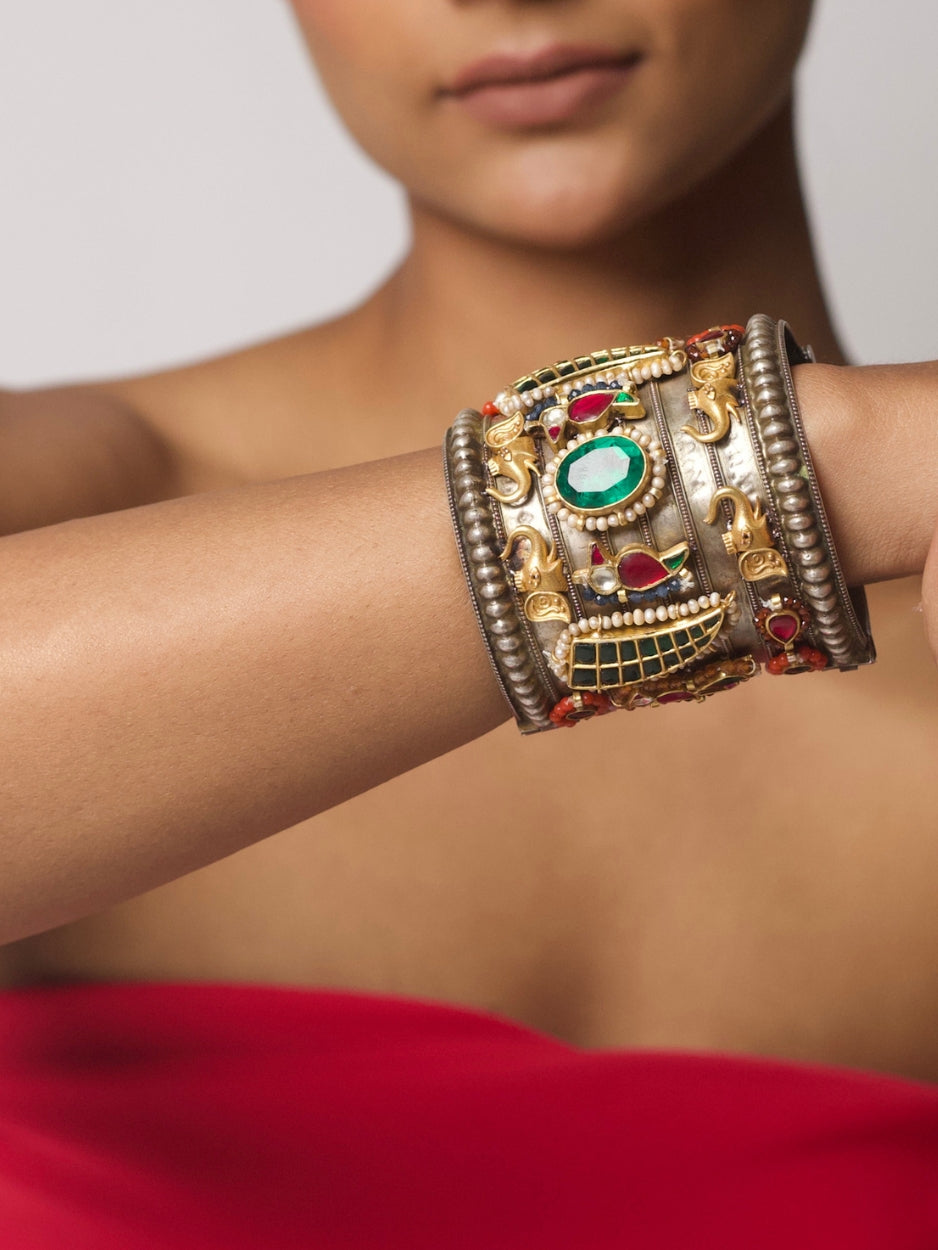 Close-up of Bazaar Relic Cuff in 92.5 silver featuring tribal base, gold motifs, emerald green stone, pearls, and red-green tikdas — worn on wrist