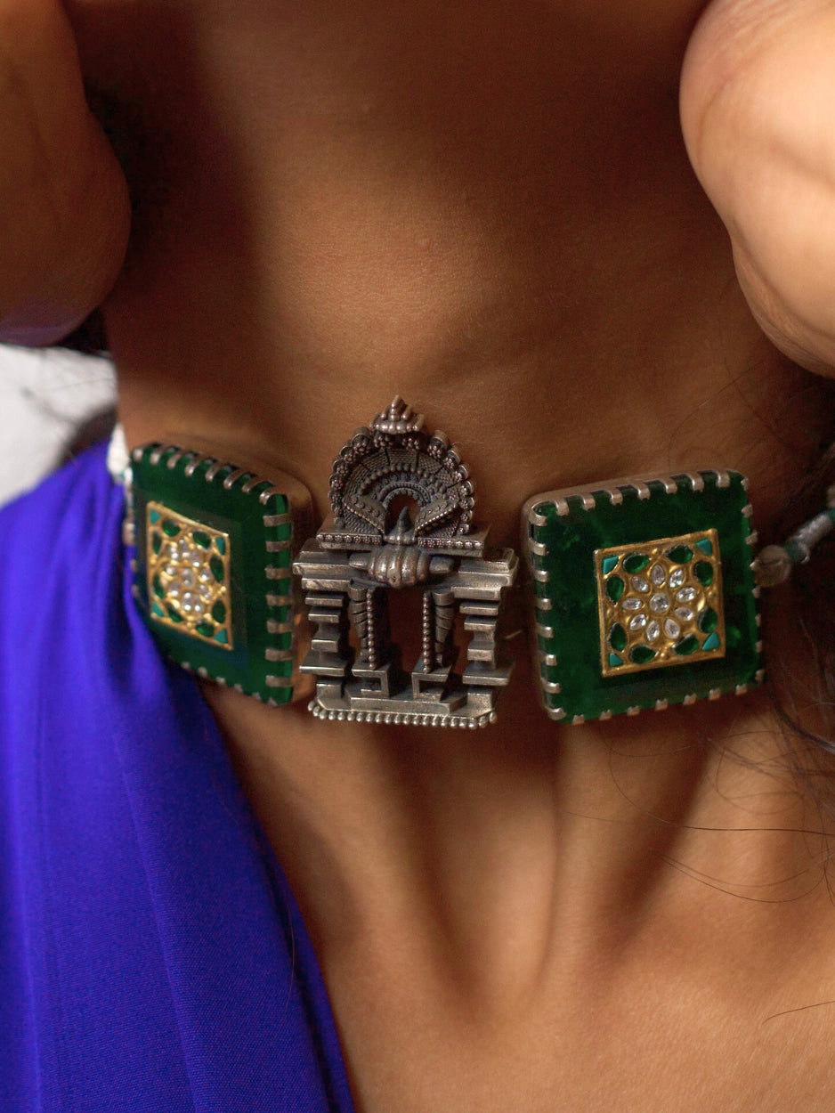 Handcrafted 92.5 silver temple choker with green enamel squares, kundan inlay, and central shrine-style motif, worn on neck against purple fabric background.