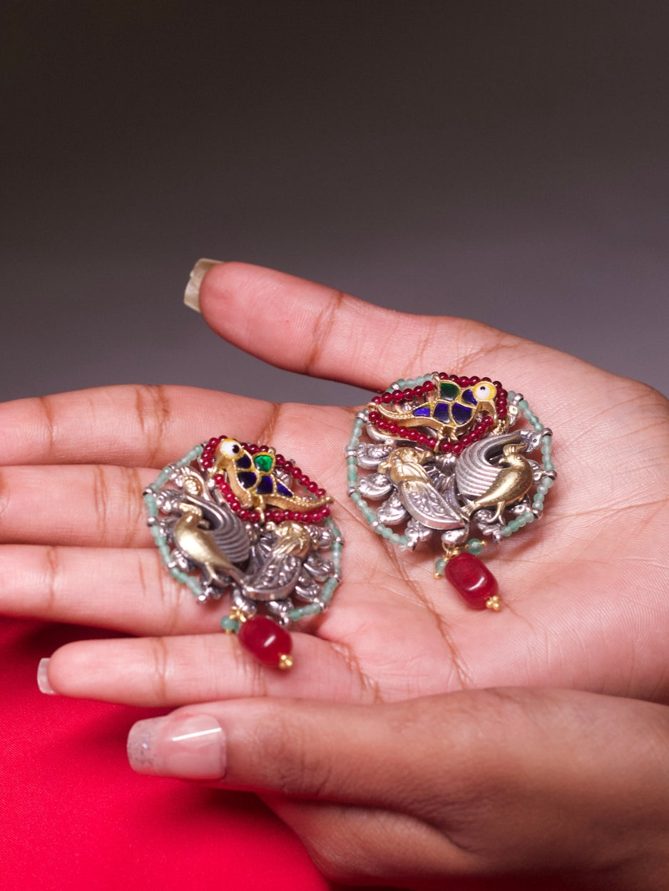 Close-up of statement 92.5 silver earrings featuring bird motifs in two-tone silver-gold and kundan-style colored enamel, bordered with mint green beads and a dangling red bead drop.