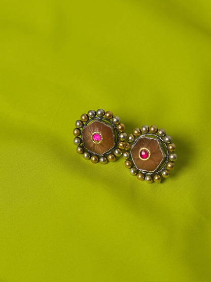 Close-up of handmade 925 silver Mango Pudding Studs with golden and silver beaded frame and pink crystal centre on green fabric.
