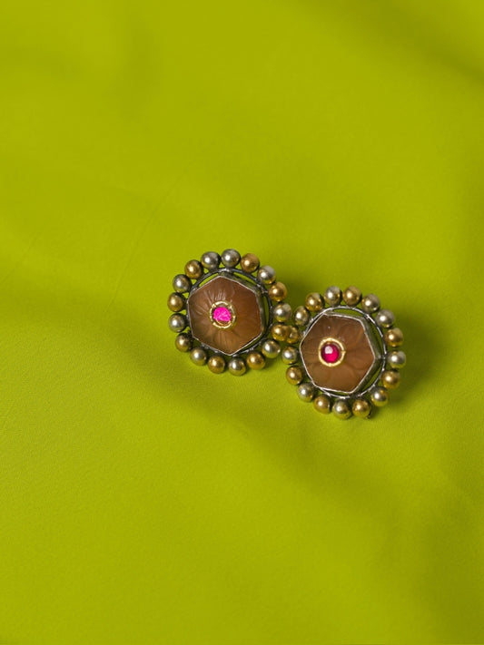 Close-up of handmade 925 silver Mango Pudding Studs with golden and silver beaded frame and pink crystal centre on green fabric.