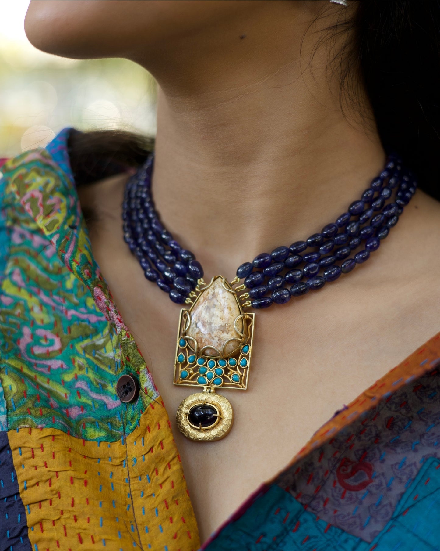 Four-strand indigo bead necklace in 925 silver with large marbled stone pendant, turquoise accents, and hammered gold drop detail.