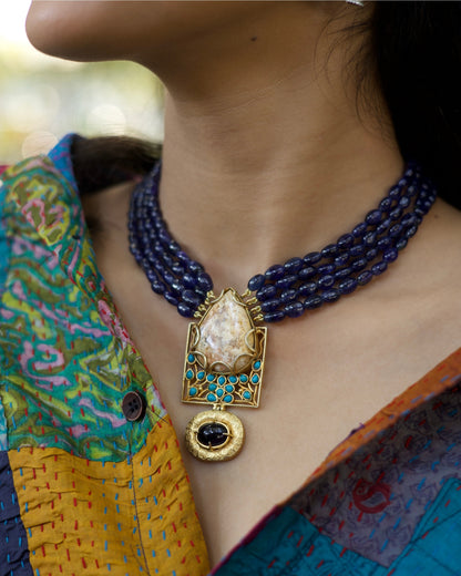 Four-strand indigo bead necklace in 925 silver with large marbled stone pendant, turquoise accents, and hammered gold drop detail.