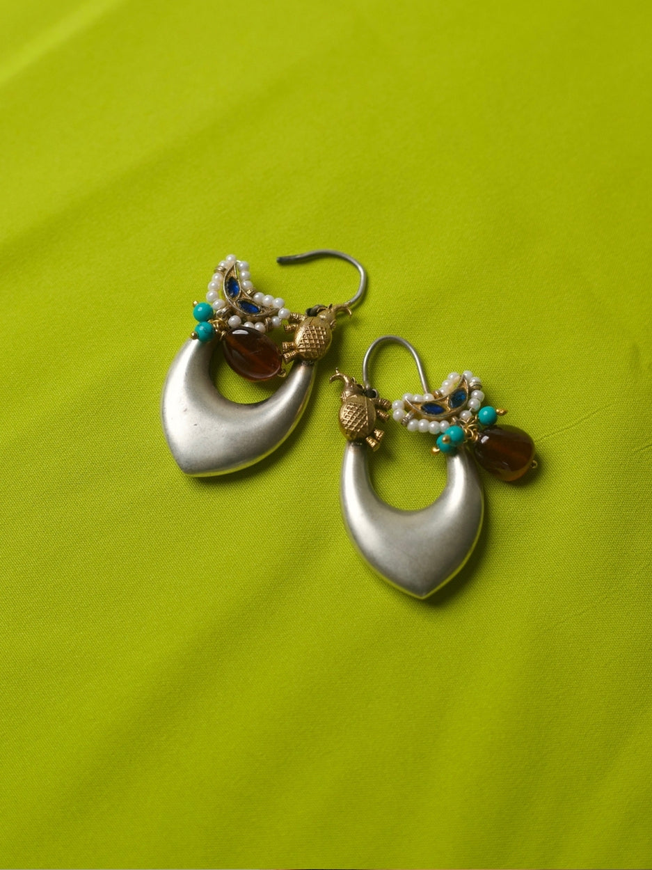 Elongated silver hoop earrings with gold elephant motifs, pearls, turquoise beads, and deep red stone charms, styled on a lime green fabric.
