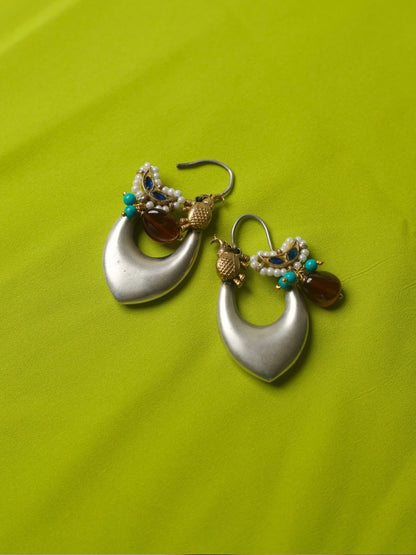 Elongated silver hoop earrings with gold elephant motifs, pearls, turquoise beads, and deep red stone charms, styled on a lime green fabric.