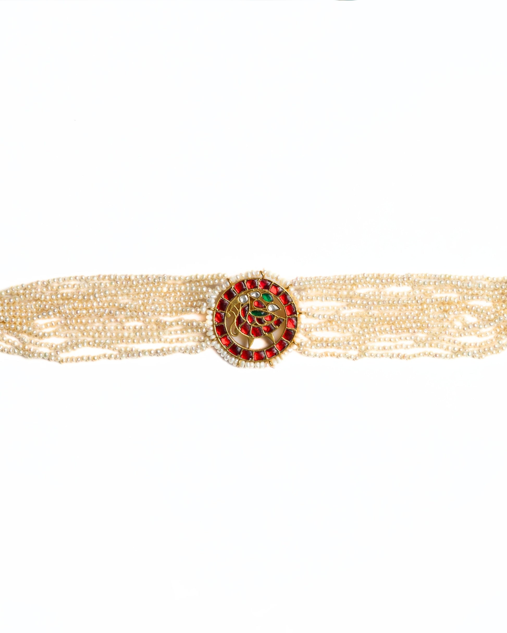 Close-up of a layered pearl choker in 925 silver with gold polish featuring a circular red stone peacock medallion at the centre.