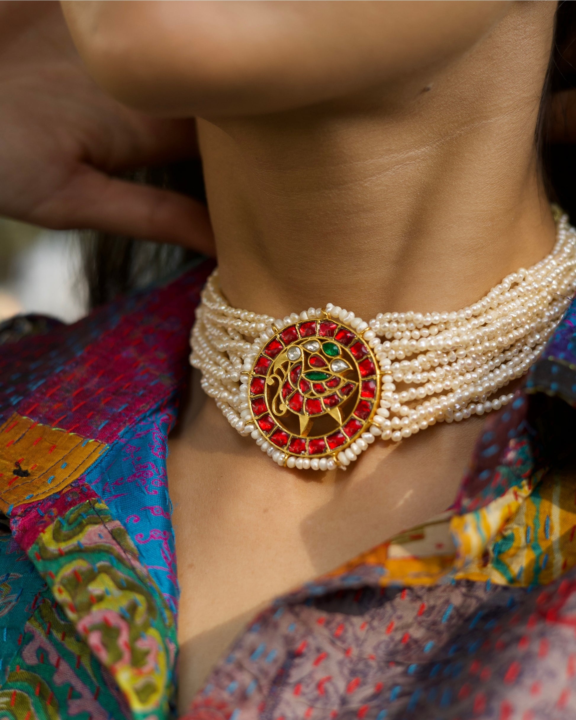 Close-up of a layered pearl choker in 925 silver with gold polish featuring a circular red stone peacock medallion at the centre.