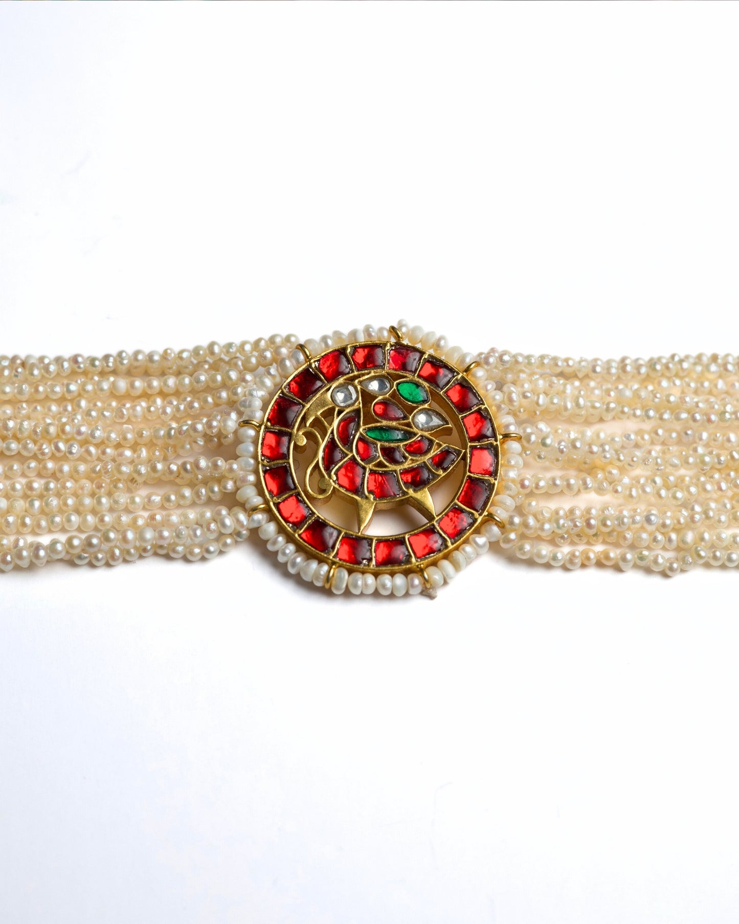 Close-up of a layered pearl choker in 925 silver with gold polish featuring a circular red stone peacock medallion at the centre.