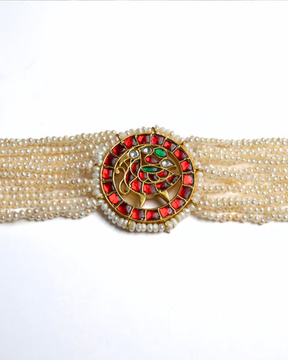 Close-up of a layered pearl choker in 925 silver with gold polish featuring a circular red stone peacock medallion at the centre.