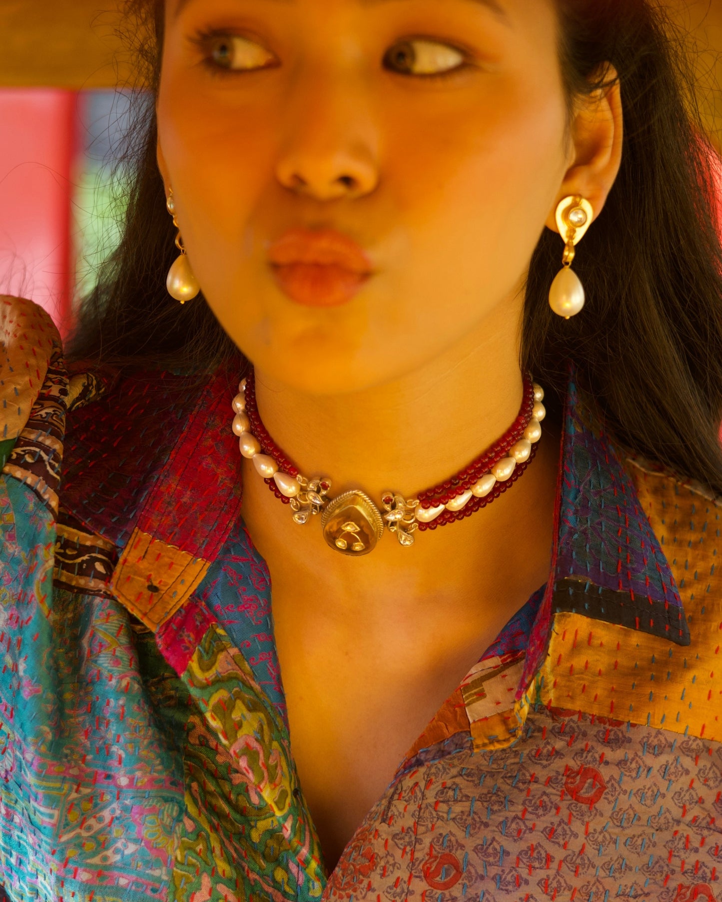 Multi-strand red bead choker in 925 silver with gold polish, pearl accents, and a large honey-toned teardrop stone centre pendant, on neck.