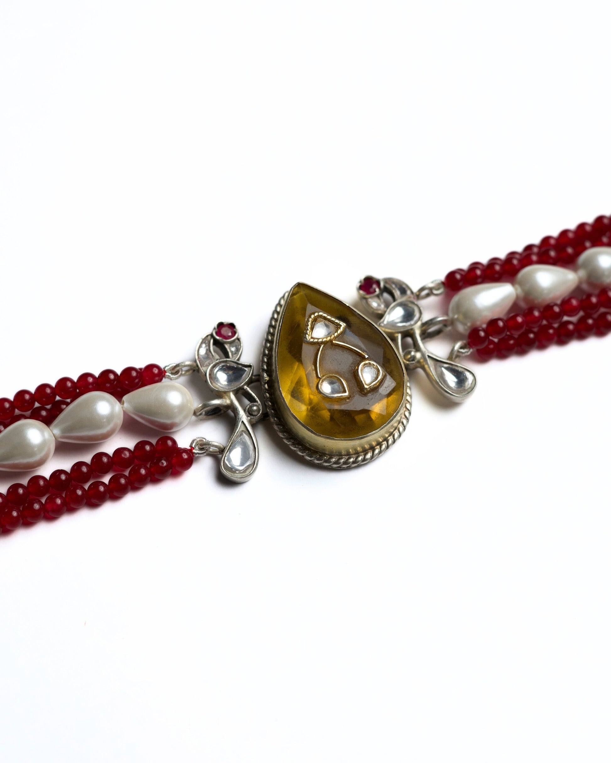 Zoomed shot of multi-strand red bead choker in 925 silver with gold polish, pearl accents, and a large honey-toned teardrop stone centre pendant.