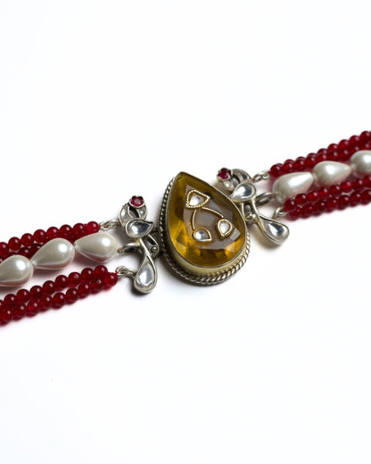 Zoomed shot of multi-strand red bead choker in 925 silver with gold polish, pearl accents, and a large honey-toned teardrop stone centre pendant.