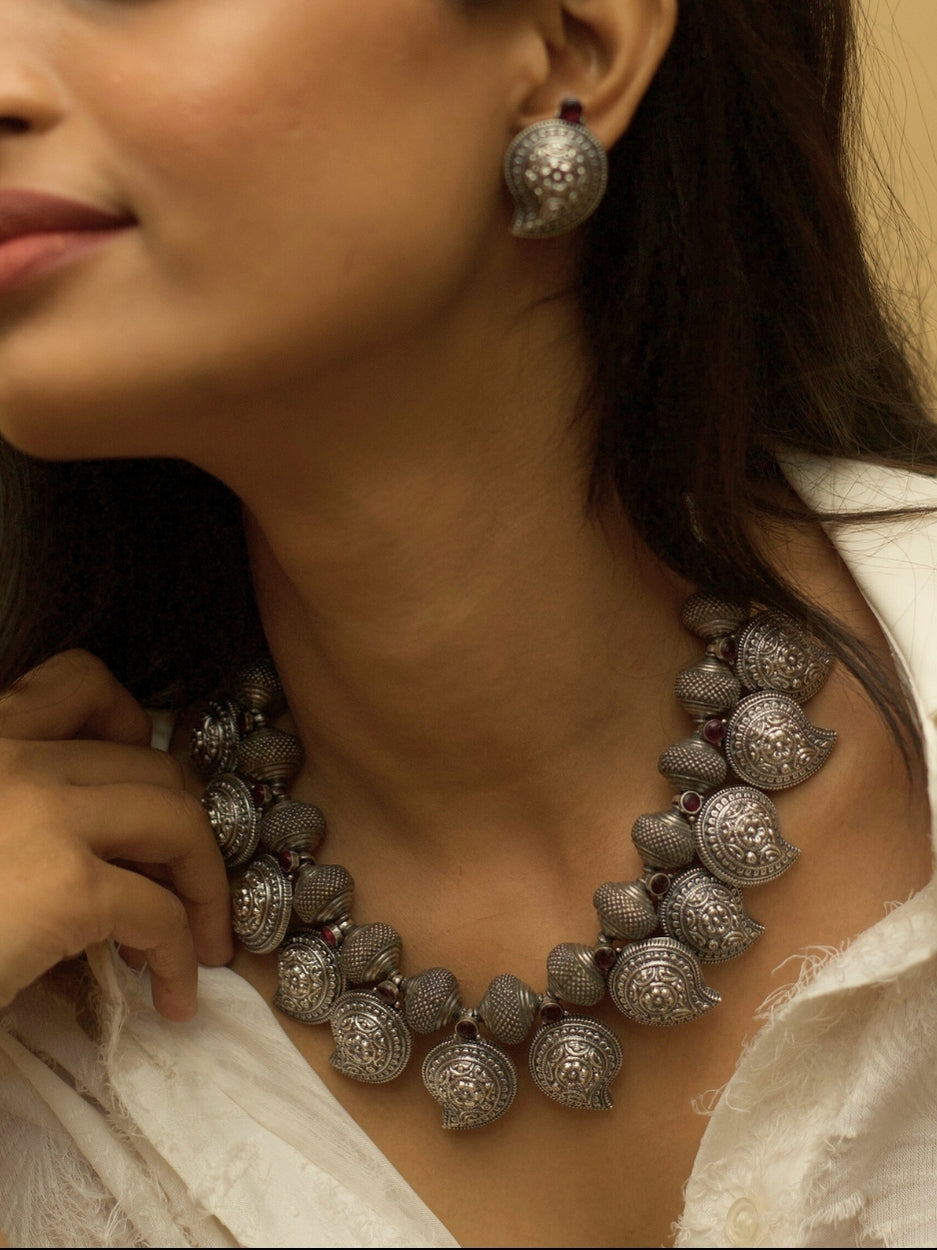 Temple Ambi Set by Naksa—oxidized 925 silver necklace and stud earrings with paisley motifs and wine-red accents.