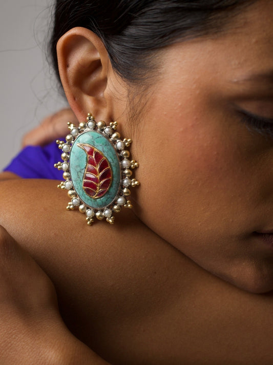 Close-up of a bold handcrafted 92.5 silver stud earring with red enamel leaf on turquoise stone, framed with pearls – worn on ear.