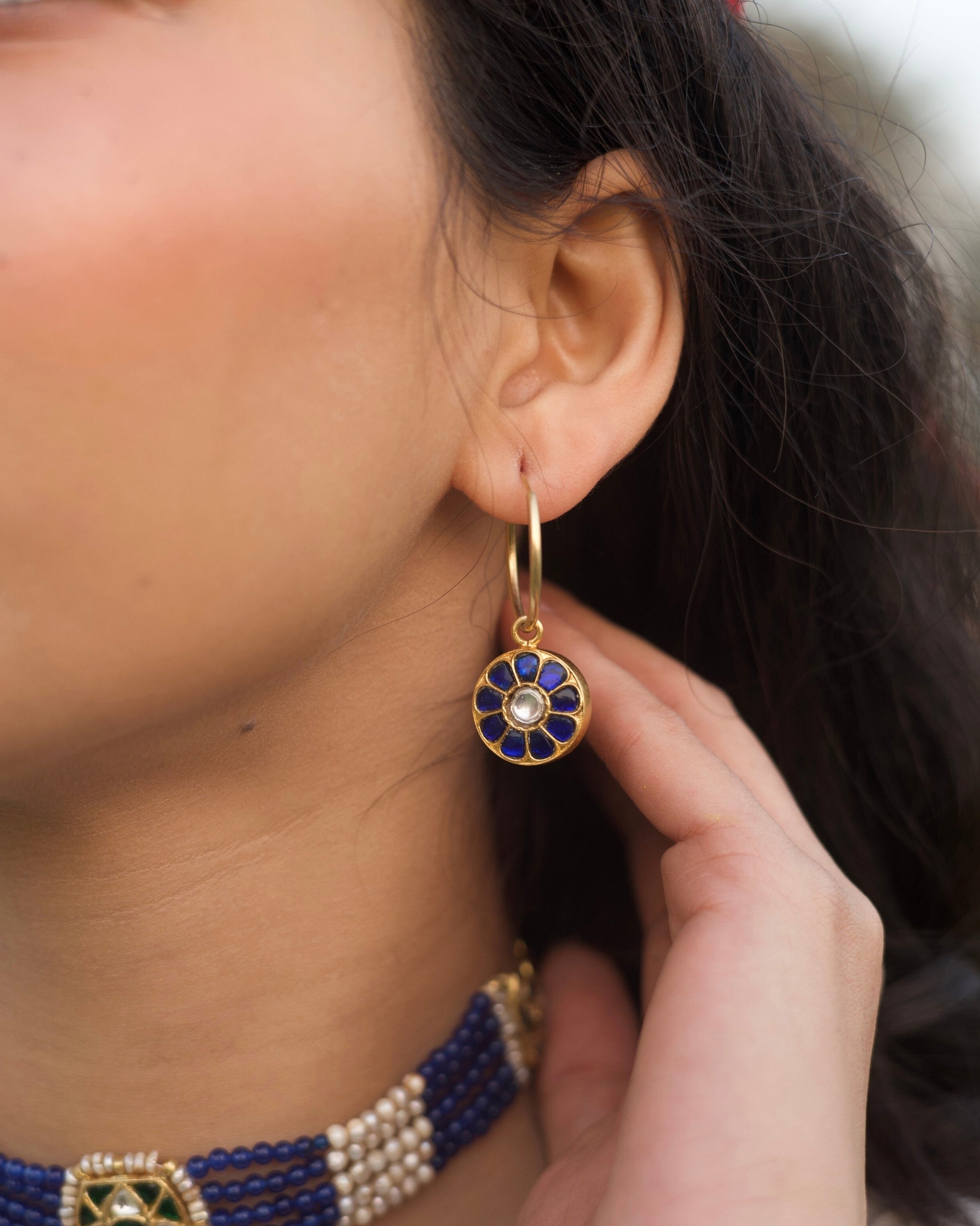 Close-up of small gold-polished 925 silver hoop earrings with deep blue lapis-style petal inlay and kundan stone centre.