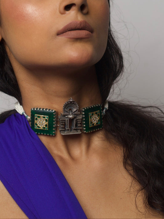 Handcrafted 92.5 silver temple choker with green enamel squares, kundan inlay, and central shrine-style motif, worn on neck against purple fabric background.