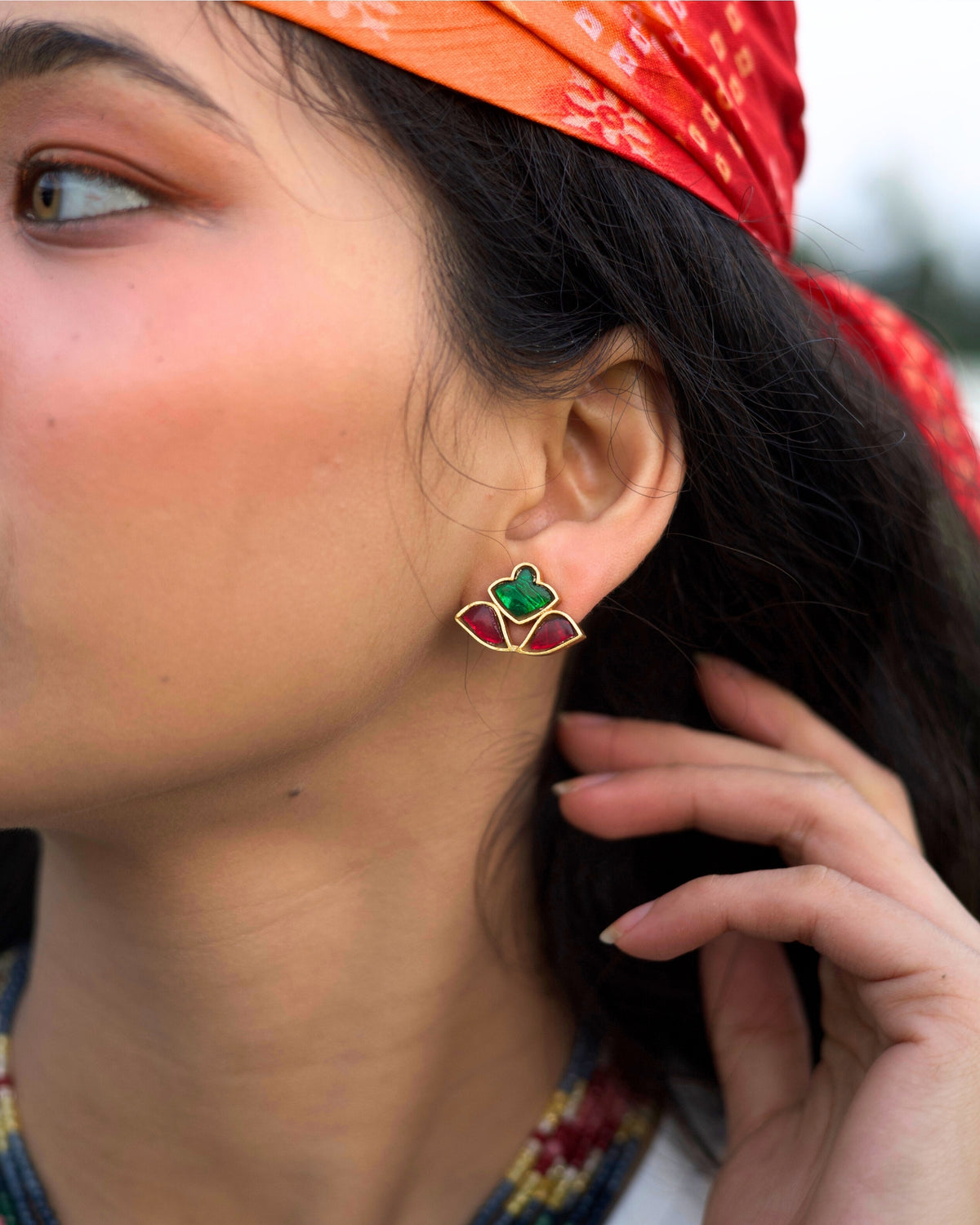 Close-up of red and green stone stud earrings in a fan-shaped mosaic design crafted in gold polished 925 silver.