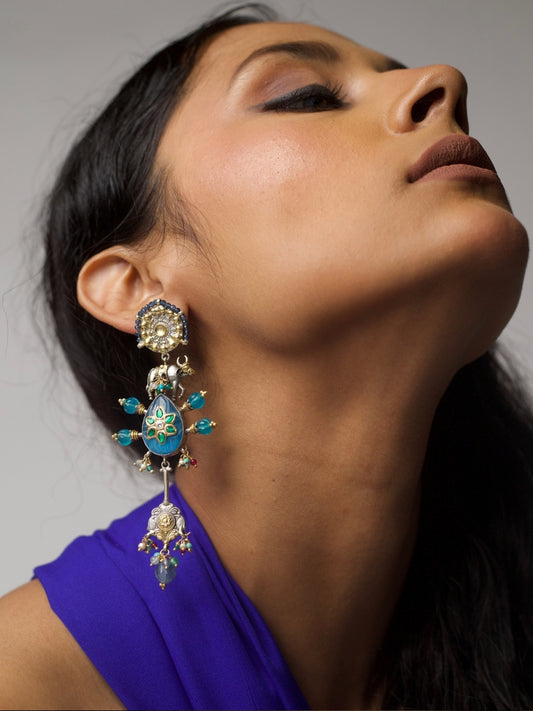Long statement earrings in 92.5 silver with gold highlights, blue enamel center, cow motifs, and dangling jhumki ends – Naksa handcrafted jewelry.