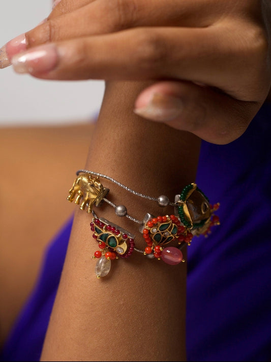 Handcrafted 92.5 silver bracelet with enamel folk charms, cow motif, and tribal bead detailing – styled on wrist against purple background.