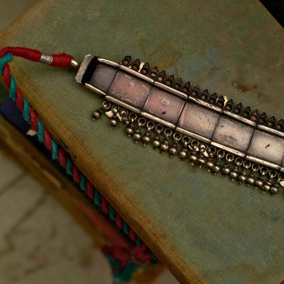 This oxidised 92.5 silver choker features three meticulously designed fish cutouts in lush pastel green, with scarlet and white gemstones on an embossed base flanked by ghunghroo beads. It comes with a shiny pink, adjustable dhaaga that perfectly complements the colours and adds a vintage charm.