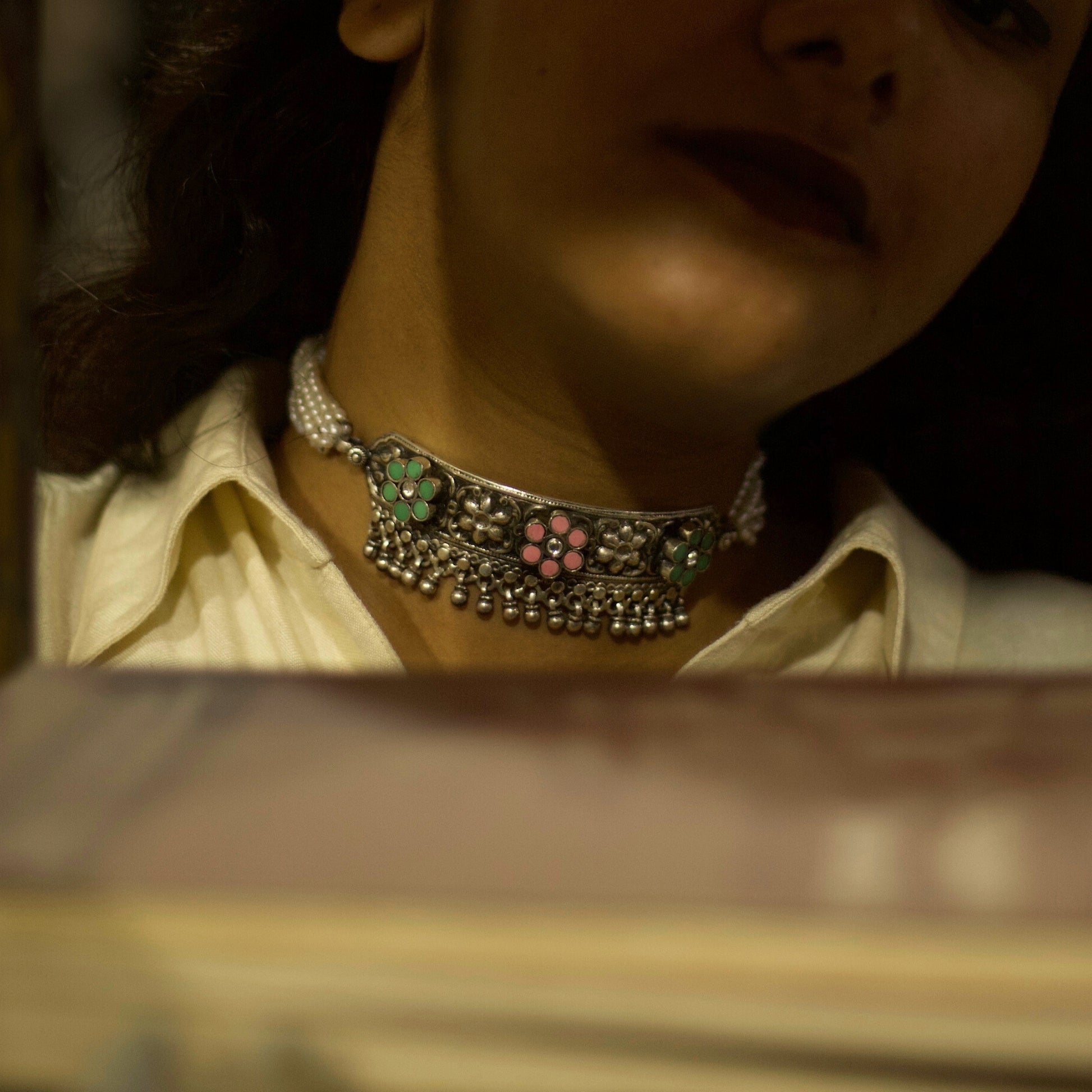 Light in weight but heavy on details, this piece creates the perfect balance by combining the dark patina of oxidised silver with pearly whites. The embossed and pastel-coloured flowers are a visual feast accentuated by the dangling ghunghroo beads. Style this with any outfit and flaunt your true spirit.&nbsp;