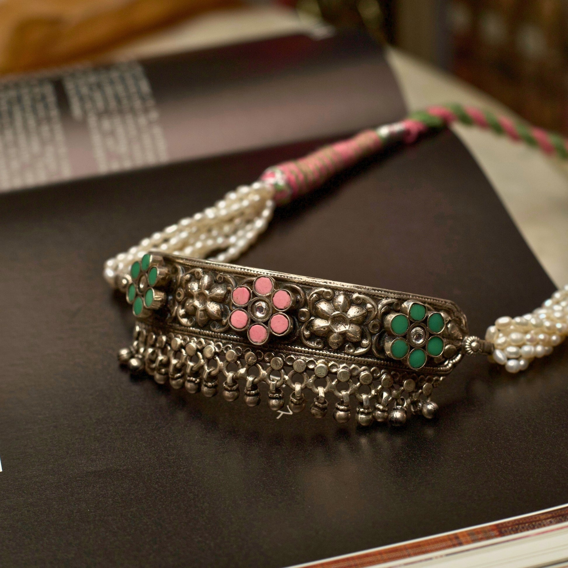 Light in weight but heavy on details, this piece creates the perfect balance by combining the dark patina of oxidised silver with pearly whites. The embossed and pastel-coloured flowers are a visual feast accentuated by the dangling ghunghroo beads. Style this with any outfit and flaunt your true spirit.&nbsp;