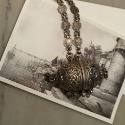 This antique silver necklace features a cylindrical box-shaped pendant with detailed engravings and&nbsp;ghunghroo beads. The chain has circles carved with the portraits of royal queens. This 925 oxidised silver necklace is a regal piece of contemporary jewellery that'll be cherished as a heirloom for years to come!&nbsp;