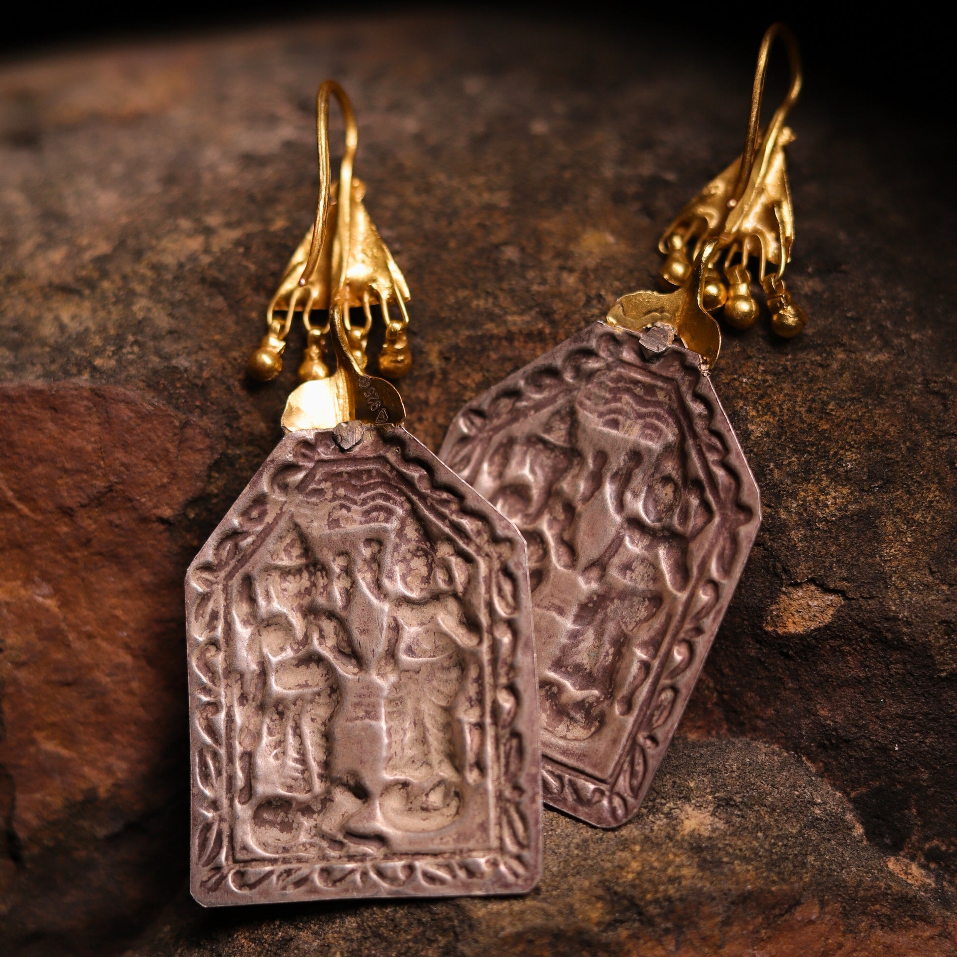 Silver earrings featuring Goddess Laxmi and Lord Ganesha embossed on antique silver pentagon plates, paired with gold-polished triangles and dangling beads resembling a mythical chariot