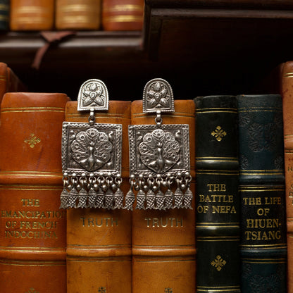 Like the arched walkways and huge doors of the Indian palaces of myths, these heritage silver earrings feature intricate engravings giving them a regal look. The centrepiece features a peacock in all its glory and dangling fish charms to complete the royal look