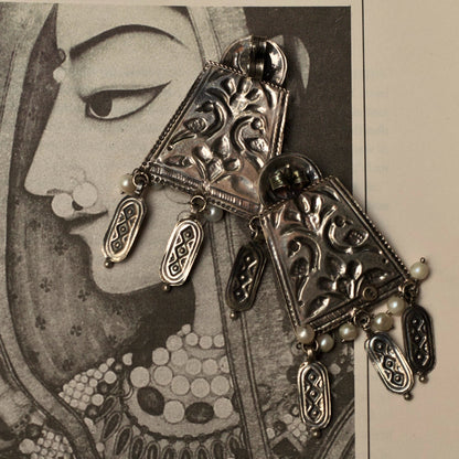 These oxidised silver earrings are a tribute to the ageless charm of Indian women told through great classic and contemporary stories. They feature a round stud engraved with the lotus, an asymmetric shape with dangling elements and thoughtful pearl work that make it hard to miss.