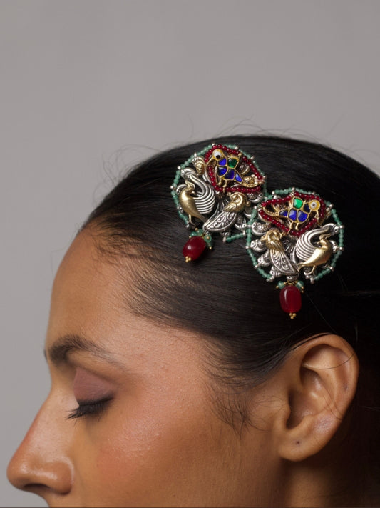 Close-up of statement 92.5 silver earrings featuring bird motifs in two-tone silver-gold and kundan-style colored enamel, bordered with mint green beads and a dangling red bead drop.