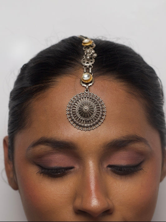 Close-up of Surya Chakra maang tikka in pure 92.5 silver with antique finish and kundan accents worn on forehead