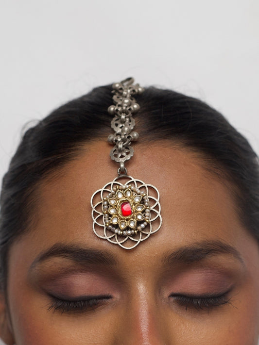 close-up of Red Reverie Tikka with red stone centerpiece, pearls, kundan and pure silver chain, worn on model's forehead